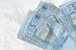 5 Ukrainian hryvnias bills lies in stack on background of big semi-transparent banknote. Abstract presentation of national currency photo