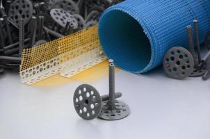 A set of construction items for the insulation of walls. Plastic dowels, a roll of mesh for the insulation of facades and a corner profile with a grid lie on the foam polystyrene surface photo