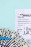 1040 tax form lies near hundred dollar bills and blue pen on a light blue background. US Individual income tax return photo