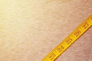 Yellow measuring tape lies on a gray knitted fabric photo