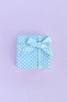 Small blue gift box with ribbon lies on a violet background. Minimalism flat lay top view photo