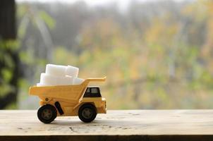 A small yellow toy truck is loaded with white sugar cubes. A car on a wooden surface against a background of autumn forest. Extraction and transportation of sugar photo