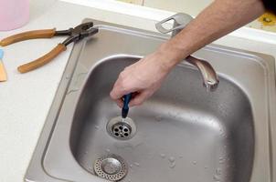 primer plano de las manos de un plomero guapo reparando el desagüe del fregadero de la cocina foto