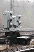 Photo of a fragment of a railway track with a small traffic light in rainy weather