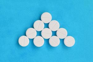 Several white tablets lie on a bright blue background in the form of a triangular arrow. Background image on medicine and pharmaceutical topics photo