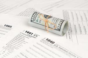 Tax forms lies near roll of hundred dollar bills. Income tax return photo