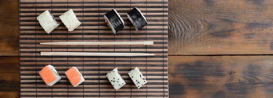 Sushi rolls and wooden chopsticks lie on a bamboo straw serwing mat. Traditional Asian food. Top view photo