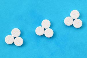 Several white tablets lie on a bright blue background in the form of three triangular arrows. Background image on medicine and pharmaceutical topics photo