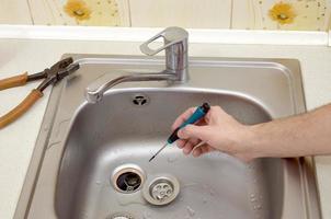 Close-up of handsome plumber hands repairing drain of kitchen sink photo