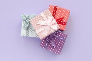 Pile of a small colored gift boxes with ribbons lies on a violet background. Minimalism flat lay top view photo