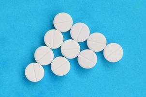 Several white tablets lie on a bright blue background in the form of a triangular arrow. Background image on medicine and pharmaceutical topics photo