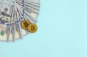 Golden bitcoins and hundred dollar bills lies on light blue background photo