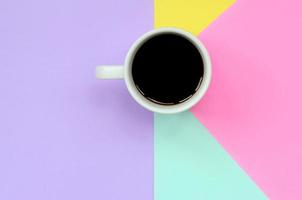 pequeña taza de café con leche sobre fondo de textura de papel de colores azul pastel, amarillo, violeta y rosa de moda en un concepto mínimo foto