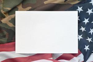 Blank paper lies on United States of America flag and folded military uniform jacket. Military symbols conceptual background banner and copy space photo