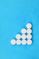 Several white tablets lie on a bright blue background in the form of a triangular arrow. Background image on medicine and pharmaceutical topics photo