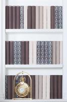 Large white bookshelf with many books of different colors and golden clock