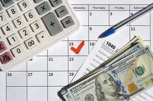 1040 declaración de impuestos sobre la renta individual en blanco con billetes de dólar, calculadora y bolígrafo en la página del calendario con el 15 de abril marcado foto