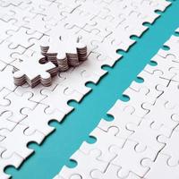 The blue path is laid on the platform of a white folded jigsaw puzzle. The missing elements of the puzzle are stacked nearby. Texture image with space for text photo