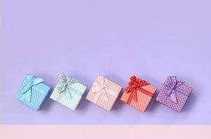 pequeñas cajas de regalo de diferentes colores con cintas se encuentran sobre un fondo de color violeta y rosa foto