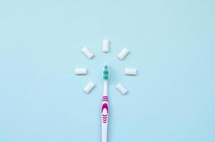 Toothbrush and chewing gums lie on a pastel blue background. Top view, flat lay. Minimal concept photo