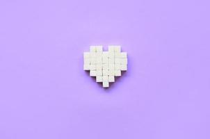 un corazón hecho de cubos de azúcar yace sobre un moderno fondo violeta pastel foto