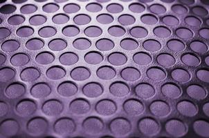 Black metal computer case panel mesh with holes on purple background. Abstract close up photo
