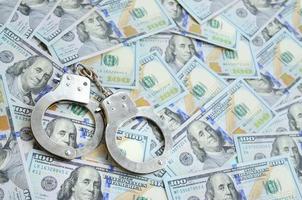 Silver police handcuffs lies on a many dollar bills photo