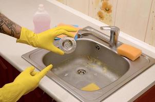 el limpiador con guantes de goma muestra un protector de desagüe limpio de un fregadero de cocina foto