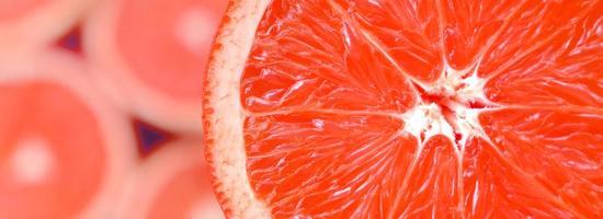 Top view of a fragment of the red grapefruit slice on the background of many blurred grapefruit slices. A saturated citrus texture image photo