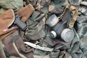 Stalker soldiers soviet gas mask lies with handgun and knife on green khaki camouflage jackets photo