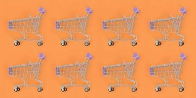Shopping addiction, shopping lover or shopaholic concept. Many small empty shopping carts perform a pattern on a pastel colored paper background. Flat lay composition, top view photo
