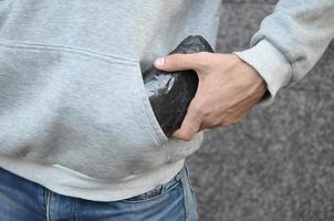 Traficante de drogas sacando una bolsa con cocaína del bolsillo de la sudadera con capucha sobre fondo de azulejos oscuros de cerca foto
