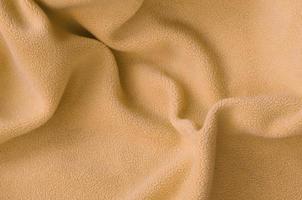 The blanket of furry orange fleece fabric. A background of light orange soft plush fleece material with a lot of relief folds photo