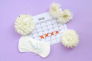 Menstrual pads and tampons on menstruation period calendar with white flowers on lilac background photo