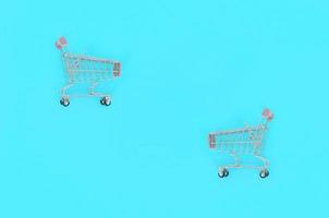 Shopping addiction, shopping lover or shopaholic concept. Small empty shopping cart lies on a pastel colored paper background. Flat lay minimal composition, top view photo