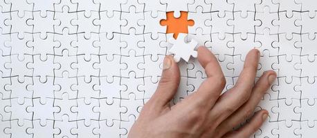 The texture of a white jigsaw puzzle in the assembled state with one missing element that the male hand puts in photo