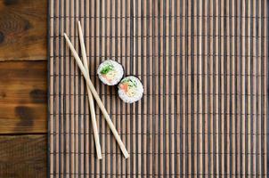 Sushi rolls and wooden chopsticks lie on a bamboo straw serwing mat. Traditional Asian food. Top view. Flat lay minimalism shot with copy space photo