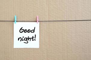 Good night Note is written on a white sticker that hangs with a clothespin on a rope on a background of brown cardboard photo