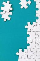 Fragment of a folded white jigsaw puzzle and a pile of uncombed puzzle elements against the background of a blue surface. Texture photo with space for text