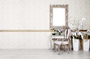 A fragment of a retro interior with a chair and table, on which is a telephone and a vase of flowers. Above the table hangs an empty picture frame for your photo