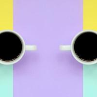 Two small white coffee cups on texture background of fashion pastel blue, yellow, violet and pink colors paper in minimal concept photo