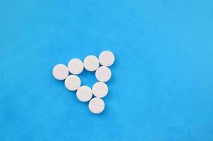 Several white tablets lie on a bright blue background in the form of an even triangle. Background image on medicine and pharmaceutical topics photo