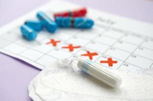 Menstrual pads and tampons on menstruation period calendar with red cross marks lies on lilac background photo