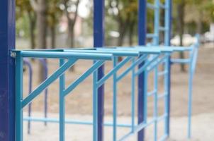 Blue metal pipes and cross-bars against a street sports field for training in athletics. Outdoor athletic gym equipment. Macro photo with selective focus and extremely blurred background