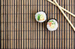 Sushi rolls and wooden chopsticks lie on a bamboo straw serwing mat. Traditional Asian food. Top view. Flat lay minimalism shot with copy space photo