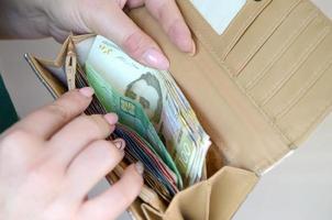 manos femeninas sosteniendo billetes de hryvnia ucraniana en una pequeña bolsa de dinero o billetera foto