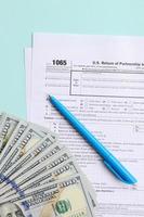 1065 tax form lies near hundred dollar bills and blue pen on a light blue background. US Return for parentship income photo