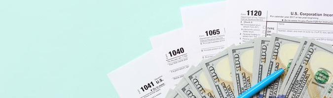 Tax forms lies near hundred dollar bills and blue pen on a light blue background. Income tax return photo