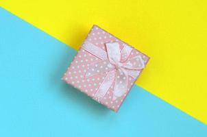 Small pink gift box lie on texture background of fashion pastel blue and yellow colors paper in minimal concept photo