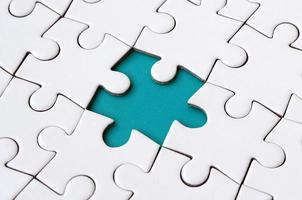 Close-up texture of a white jigsaw puzzle in assembled state with missing elements forming a blue pad for text. Copy space photo